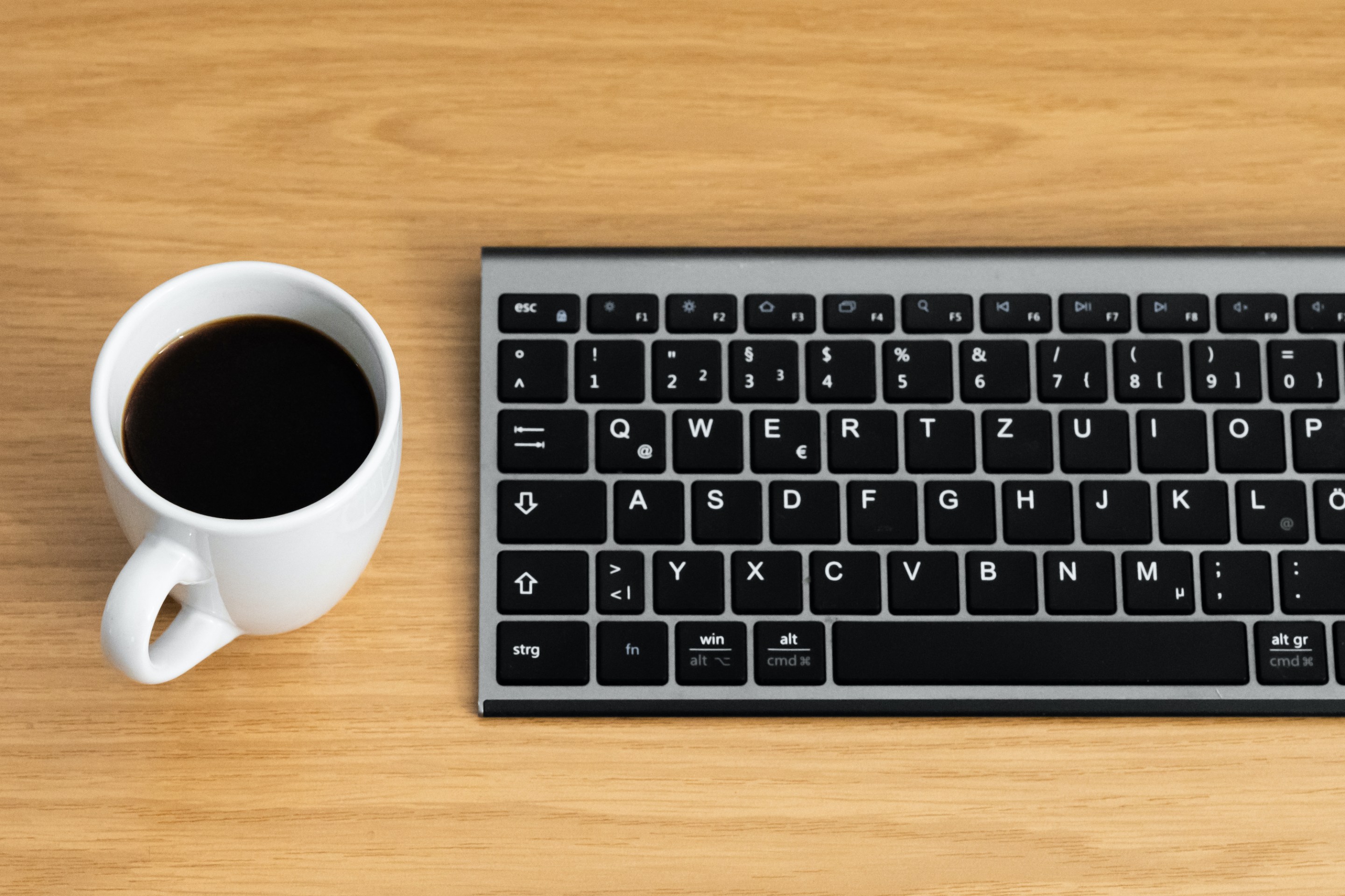 A mug of coffee next to a keyboard.